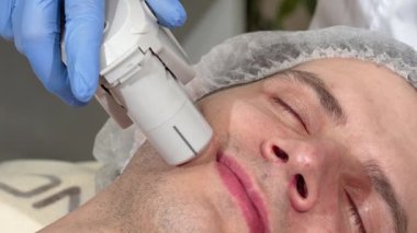 Rahat bir adam modern bir güzellik kliniğinde rahatlatıcı bir ultrason cilt tedavisiyle eğleniyor. Yetenekli bir kozmetolog cildini geliştirmek için ileri teknoloji uyguluyor. Huzurlu atmosfer ve profesyonel bakım gençleştirici etkileri vurguluyor