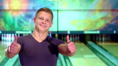 Genç beyaz bir adam, canlı bowling salonunda büyük bir sevinç saçarak başparmağını havaya kaldırdı. Renkli arka plan ve parlak şeritler bu eğlence dolu bowling deneyiminin heyecanını arttırıyor.