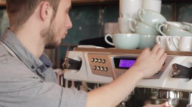 Yetenekli bir erkek barista, odaklanmış bir ifadeyle, etrafı düzgünce istiflenmiş fincanlarla çevrili bir kahve makinesini ustalıkla çalıştırıyor. Bu canlı sahne, kahve kültürünün özünü yakalar. İçilen her fincanın arkasındaki sanat ve tutkuyu gözler önüne serer.