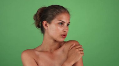 Güneş yanığı tenli çarpıcı genç bir kadın zarif poz veriyor, doğal güzelliğini canlı yeşil bir arka planda sergiliyor. Onun çıplak omuzları ve kendinden emin bakışları şehvet ve zarafet saçıyor, hayranlık ve takdir uyandırıyor.