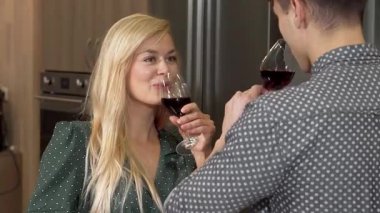 Uzun sarı saçlı neşeli bir kadın kırmızı şarap kadehini kaldırıyor ve şık bir mutfakta erkek arkadaşıyla özel bir anı kutluyor. Sıcak atmosfer ve onların sevgi dolu gülümsemeleri mükemmel bir sevgililer günü atmosferi yaratır.