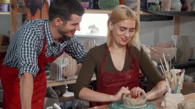 Neşeli genç bir kadın ve erkek arkadaşı seramik kaseyi elleriyle ustalıkla şekillendirerek çömlek sanatına daldılar. Renkli aletlerle ve sanatsal yaratıklarla çevrelenmiş olan bu kahkahalar havayı dolduruyor, sevgi ve yaratıcılığı somutlaştırıyor.