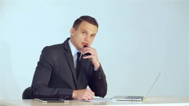 Sivri takım elbiseli genç bir erkek işadamı, telefonda dikkatle dinliyor, profesyonelliğini ve nişanını gösteriyor. Düşünceli ifadesi ve modern ofis yapısı kurumsal iletişim ve işbirliğinin dinamik doğasını vurguluyor.