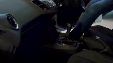 Odaklanmış beyaz bir adam araba sürmeye hazırlanıyor, emniyet kemerini kararlılıkla bağlıyor. Yakın plan, modern bir arabanın içinde güvenlik ve hazırlığı vurgulayarak elini hareket halinde yakalıyor.