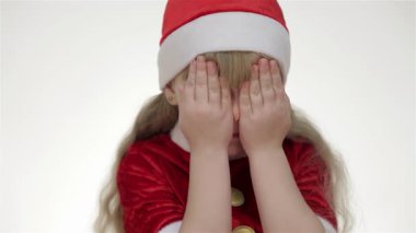 Neşeli bir Noel Baba şapkası takmış neşeli bir kız çocuğu, parlak bir stüdyo ortamında yürekten gülerken neşe saçıyor. Yumuşak beyaz bir arka planla çevrili, Noel ruhunu somutlaştırıyor, saate bakarken oyuncak ayıya şakayla sarılıyor.