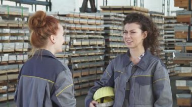 İki hevesli kadın fabrika işçisi neşe dolu bir beşliği paylaşıyor, gülümsemeleri neşe saçan bir depoda düzgünce istiflenmiş malzemelerle dolup taşıyor. Bu canlı sahne, takım çalışmasının ve başarının özünü yansıtıyor.