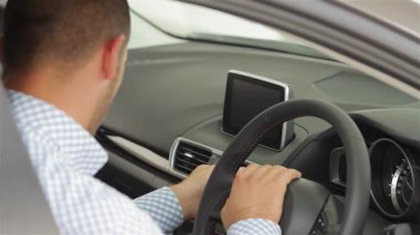 Genç bir adam lüks lüks bir arabanın direksiyonunda güvenle oturuyor ve son model otomotiv teknolojisini sergiliyor. Onun odaklanmış ifadesi ve modern gösterge paneli potansiyel alıcılar için davetkar bir atmosfer yaratarak,