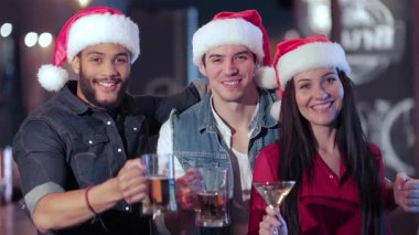 Neşeli bir üçlü, iki erkek ve bir kadın, neşeli bir barda içkilerini yudumlarken Noel Baba şapkaları giyerler. Atmosfer kahkaha ve arkadaşlıkla dolu. Bayram ruhunun tadını çıkarıyorlar.