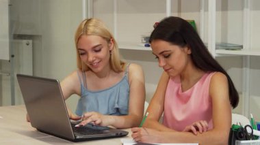 İki neşeli genç kadın, parlak ve modern bir çalışma alanında dizüstü bilgisayarla uğraşırken gülücüklerini ve fikirlerini paylaşarak bir projede işbirliği yapıyorlar. Enerjik enerjileri ve takım çalışmaları, akademik bir ortamda öğrenmenin ve arkadaşlığın neşesini vurguluyor.