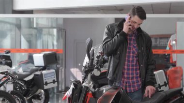 Neşeli beyaz bir adam modern bir bayilikte çarpan siyah bir motosikletin yanında dururken bir telefon görüşmesi yapar. Günlük ekose gömleği ve deri ceketi motosikletlerin şık tasarımını tamamlıyor ve davetkar bir atmosfer yaratıyor.