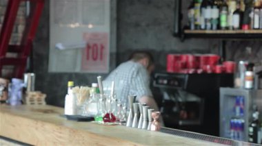 Şık, sarışın bir adam, sıradan bir tişört giymiş, canlı bar tezgahında soğuk bir bira sipariş etmek için kolunu kaldırıyor. Atmosfer canlı, renkli şişelerden oluşan bir zemin ve hizmet etmeye hazır dost bir barmen, mükemmel bir...