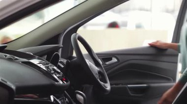 Genç bir kadın hareketli bir galeride lüks bir arabanın içinde oturuyor, dikkatle kontrolleri heyecan dolu bir bakışla ayarlıyor. Bu canlı sahne araba alışverişinin heyecanını yakalıyor, modern otomotiv deneyimini ve mutluluğunu sergiliyor.