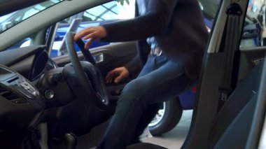 Sakallı, yakışıklı beyaz bir adam kemerini şık bir otomobilin içine takarken parlak bir şekilde gülümsüyor. Arabanın canlı iç tasarımı ve modern tasarımı onun yeni sürüş macerasının heyecanını arttırıyor.