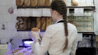 Gıcır gıcır beyaz gömlek ve önlük giymiş neşeli genç bir fırıncı büyüleyici bir kahve dükkanında altın bir somun ekmek sunuyor. Davetkar atmosfer taze pişmiş hamur işlerinin enfes aromasıyla doludur. Müşterileri cezbedici bir şekilde cezbeder.