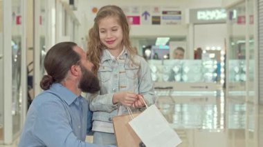 Dalgalı saçları ve kot ceketi olan neşeli küçük bir kız heyecan verici bir şeye işaret ediyor, canlı bir alışveriş merkezinde babasının dikkatini çekiyor. Bu iç açıcı sahne, sakallı bir baba ile babası arasındaki özel bağı gözler önüne seriyor.