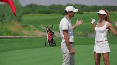 Karizmatik bir erkek golf hocası golfün karmaşıklığını onunla şakalaşarak nişanlanan kızıl saçlı güzel bir kadına anlatırken coşkuyla el kol hareketi yapar. Bereketli yeşil bir golf sahasının karşısında canlı etkileşimleri sıcaklığı ve sıcaklığı yansıtıyor.