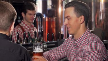Şık, neşeli bir adam lezzetli birasından bir yudum alır ve hareketli bir barda arkadaşıyla canlı sohbete girişir. Sıcak ortam ve şık dekor bu dostluk ve rahatlama kutlaması için mükemmel bir zemin oluşturuyor.