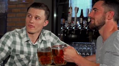İki neşeli erkek arkadaş barda heyecanlı bir futbol maçı izlerken kahkaha ve heyecanı paylaşıyor, her biri soğuk bir bardak bira tutuyor. Hayat dolu atmosfer, dostluk ve neşe ile dolu. Bu da onu unutulmaz bir ortam haline getiriyor.