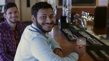 Canlı bir yukarıdan bakıldığında, biri sakallı, diğeri ekose gömlekli iki neşeli genç adam görülüyor. Kahkahalarını ve hikayelerini, hareketli bir barda soğuk bira eşliğinde paylaşıyorlar. Bu canlı sahne dostluğu ve kutlamayı simgeliyor, güzel zamanların şerefine.