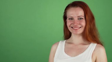 Genç ve çekici bir kadının canlı bir stüdyo portresi dalgalı kızıl saçlı, parlak bir şekilde gülümseyen ellerini uzatarak davet edici bir kopya alanı gösteriyor. Neşeli ifadesi ve zarif duruşu çekici bir atmosfer yaratıyor.