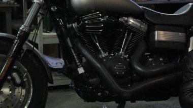 Şık sakallı beyaz bir adam hareketli bir motosiklet atölyesinin zemininde oturmuş akıllı telefonuyla yazı yazıyor. Parlak krom ve güçlü makinelerle çevrelenmiş, bisiklet kültürü tutkusunu somutlaştırıyor.