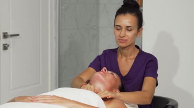 Yetenekli bir kadın terapist olgun müşterisine nazikçe yatıştırıcı bir yüz masajı yapar. Huzur ve bakım yayar. Yumuşak ışıklandırma ve sakinleştirici renk paletiyle vurgulanan sakin atmosfer canlandırıcı deneyimi güçlendirir.