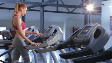 Göz kamaştırıcı kızıl saçlı bir kadın koşu bandına güvenle yaklaşır parmakları hareketli fitness merkezindeki makineyi çalıştırmak için hazırdır. Canlı pembe bir bluz ve parlak gri taytlar giymişti. Sağlıklı bir yaşam tarzına sahipti. Yola çıkmaya hazırdı.