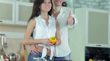 Neşeli bir çift, neşeli bir mutfakta canlı bir yemek pişirme seansından zevk alır, kız neşeli bir şekilde dans ederken canlı sarı bir biber tutar. Gülümsemeleri mutluluk saçıyor. Taze malzemeler hazırlıyorlar. Yemek pişirmenin sevincini gösteriyorlar.