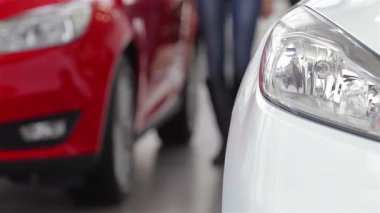 Hareketli bir otomobil galerisinde, genç bir kadın göz alıcı kırmızı araçlarla çevrili parlak beyaz bir arabayı inceliyor. Bu canlı otomotiv sahnesi araba alışverişinin heyecanını yakalıyor, teknoloji ve kişisel tercihler arasındaki etkileşimi vurguluyor.