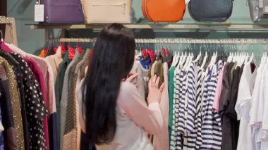 Canlı bir moda butiğini keşfederken kameraya uzun siyah saçlı çekici bir kadın. Renkli giysiler ve modaya uygun aksesuarlarla çevrelenmiş halde perakende terapi zevkini somutlaştırıyor.