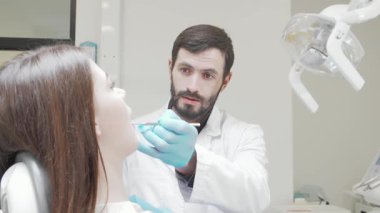 Beyaz önlüklü ve mavi eldivenli kendini işine adamış bir dişçi modern bir klinikte genç bir kadının dişlerini dikkatle inceliyor. Bu samimi an diş bakımının önemini ve hasta ile profesyonel arasındaki güveni vurguluyor.