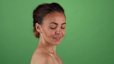 Göz kamaştırıcı genç bir kadın, parlak yeşil renkli bir arka plana zarif bir şekilde poz vererek neşe saçıyor. Kusursuz cildini sergiliyor. Çekici gülüşü ve zarif tavırları izleyicileri kendine güvenin ve kadınlığın güzelliğini takdir etmeye davet ediyor.