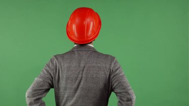 Çevresini parlak yeşil bir krom arka planla gözetleyen, canlı kırmızı bir şapkayla odaklanmış bir erkek müteahhidin dikiz görüntüsü. Bu çarpıcı görüntü mühendislik ve yenilik ruhunu somutlaştırıyor, profesyonelliğin karışımını gösteriyor.