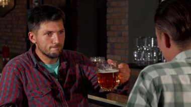 Olgun sakallı bir adam köpüklü bir biradan hoşlanır, samimi bir barda arkadaşıyla derinden bir sohbete dalmıştır. Sıcak ortam ve taşralı tuğla zemin, arkadaşlığın ve dostluğun canlı atmosferini artırıyor.