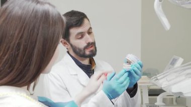 Becerikli bir dişçi, dişçi muayenesi sırasında özenli kadın hastasını detaylı bir diş kalıbını göstererek tutkuyla eğitir. Bu etkileşim, ağız sağlığı ve hasta bakımının modern ve iyi donanımlı...