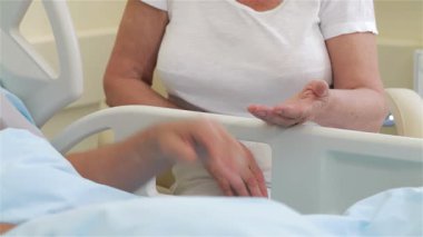 Yaşlı ve hasta bir adamın elini karısının avucuna koyup sarsılmaz desteği sembolize ettiği hassas bir an yaşanıyor. Birbirlerine dolanmış ellerini yakalıyorlar, hastane yatağının yanında sıcaklık ve bağlantı yayıyorlar, derin bağlarını gösteriyorlar.