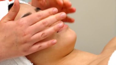 Yetenekli bir masaj uzmanı, sakin bir güzellik salonunda genç bir kızın alnını nazikçe okşayarak rahatlatıcı bir atmosfer yaratıyor. Yakın plan, kızların yumuşak cildinin üzerinde süzülen narin kadın ellerini yakalıyor. Rahatlık ve sükuneti ön plana çıkarıyor.