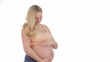 Işıl ışıl sarışın bir kadın parlak bir stüdyoda göbeğini nazikçe okşar, mutluluk ve beklenti saçar. Sıcak gülüşü anneliğin neşesini yansıtıyor. Sevgi ve beklentiyle dolu huzurlu bir atmosfer yaratıyor.