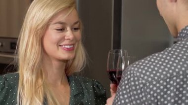 Neşeli bir kadın kırmızı şarap kadehini kaldırır, sıcak bir dairede sevgililer gününü kutlamak için sevgilisiyle tokuşturur. Gülüşleri mutluluk ve şefkat saçıyor. Romantizm için mükemmel sıcak bir atmosfer yaratıyor.