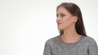 Uzun, dalgalı saçları olan neşeli bir esmer kız şakacı bir jest yapıyor, parmağını dudaklarına bastırıp yumuşak beyaz bir arka plana bastırıyor. Bu büyüleyici portre pozitiflik ve çekicilik yayıyor, gençlik ruhunu ve çekici gülümsemesini sergiliyor