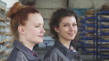 Kendine güvenen iki kadın mühendis, biri çarpıcı kızıl saçlı ve diğeri güzel bukleli, canlı bir fabrika arkaplanının ortasındaki kameraya ışıl ışıl gülümsüyor. Profesyonellikleri ve yoldaşlıkları, güçlü ve başarılı bir şekilde parlıyor.