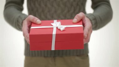 Yakından çekilen bir fotoğraf genç bir adamı yakalar, rahat, örgü örmüş bir süveter içinde, elinde narin beyaz bir kurdeleyle süslenmiş kırmızı bir hediye kutusu vardır. Bu festival anı sıcaklık ve heyecan saçıyor, kış boyunca kutlama ve aşkın ruhunu somutlaştırıyor.