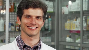 Neşeli genç bir eczacı kameraya ışıldıyor, gururla iki kabarcığı canlı haplarla dolduruyor. Düzenli eczane raflarının bir zeminine kurulmuş dostane tavrı profesyonelliği ve dünyanın güvenini ortaya koyuyor.