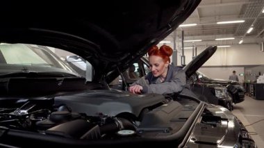 Yetenekli bir kadın araba tamircisi modern bir garajda lüks bir cipin motorunu incelerken kendine güveni tamdır. Otomotiv tamiri tutkusu, geleneksel erkek egemen mesleklerde kadınların güçlendiğini gösteriyor.