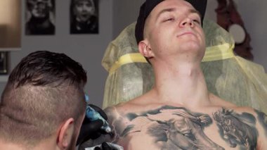 Bu dinamik çekimde, yakışıklı genç bir adam kolunda titizlikle çalışan yetenekli bir dövme sanatçısı olarak rahatça uzanır. Atmosfer rahat ama odaklanmış. Vücut mürekkebindeki ustalık ve hassasiyeti gözler önüne seriyor. Canlı tasarımlar geliyor.