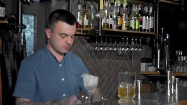 Çarpıcı dövmeleri olan yetenekli bir barmen titizlikle canlı bir kokteyl hazırlıyor ve karışımbilim konusundaki uzmanlığını gösteriyor. Canlı bar atmosferi pırıl pırıl cam eşyalar ve renkli içki şişeleri ile zenginleştirilir.