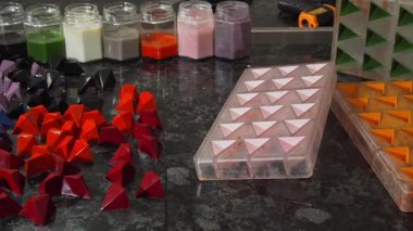 Göz kamaştırıcı renkli geometrik çikolata şekerlemeleri parlak çikolata kaplamalı kavanozlarla çevrili cilalı bir masaya yayılıyor. Bu şekerleme başyapıtı, bir çikolatacının sanatsal özelliklerini sergiliyor.