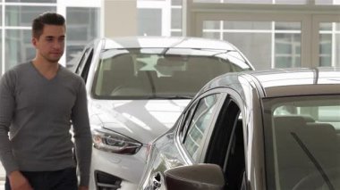 Genç bir adam parlak bir otomobil galerisinde lüks bir arabanın içini inceleyerek otomotiv teknolojisindeki en son teknolojiyi sergiliyor. Odaklanmış ifadesi, bilgili bir pazarlamacıyla ilişki kurarken heyecan ve merakı yansıtıyor.