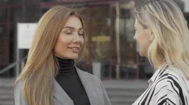 Kendine güvenen iki bayan meslektaşı, modern bir ofis binasının önünde neşeyle dışarıda sohbet ediyor ve pozitif enerji yayıyorlar. Bu canlı değişim, kadınların iş yerinde güçlenmesini ve işbirliğini sembolize ediyor. Takım çalışmasının güzelliğini gösteriyor.