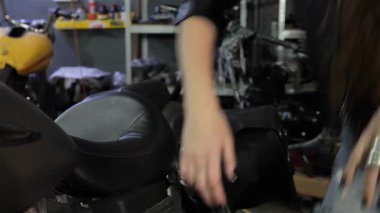 Büyüleyici genç bir bayan motorcu zarif bir şekilde zarif motosikletinin yanına çömeliyor, parmakları nazikçe benzin deposunu okşuyor. Lezzetli kıvırcık saçlarıyla şık siyah deri ceketinin üzerinde şelale gibi kıvırcık saçlarıyla kendine güveni ve cazibesi yayılıyor.